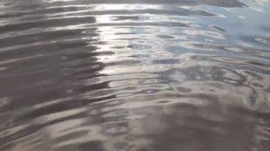 Suyun üzerinde parlama ve yansımalar. Gökyüzü suya yansıyor. Dalgaların, yansımaların, kırılmaların ve mavi, temiz ve kristal sudaki soyut kırıkların arkaplanı. Ağaçlar suya yansır..