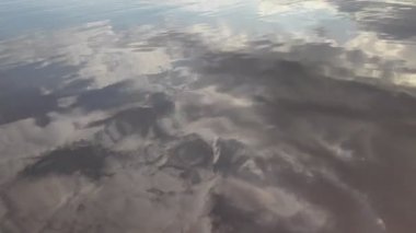 Suyun üzerinde parlama ve yansımalar. Gökyüzü suya yansıyor. Dalgaların, yansımaların, kırılmaların ve mavi, temiz ve kristal sudaki soyut kırıkların arkaplanı. Ağaçlar suya yansır..