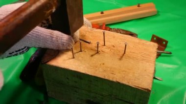 Çekiç çivisi. Çekiç ve çivi kullanarak. Tahtaya çivi çakmaya yakın. Kırmızı flanel gömlek, kot pantolon ve kumaş eldiven giyen bir marangoz tahta tahtaları çiviliyor..