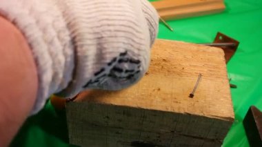 Çekiç çivisi. Çekiç ve çivi kullanarak. Tahtaya çivi çakmaya yakın. Kırmızı flanel gömlek, kot pantolon ve kumaş eldiven giyen bir marangoz tahta tahtaları çiviliyor..