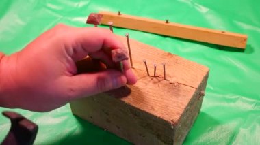 Çekiç çivisi. Çekiç ve çivi kullanarak. Tahtaya çivi çakmaya yakın. Kırmızı flanel gömlek, kot pantolon ve kumaş eldiven giyen bir marangoz tahta tahtaları çiviliyor..