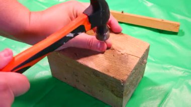 Çekiç çivisi. Çekiç ve çivi kullanarak. Tahtaya çivi çakmaya yakın. Kırmızı flanel gömlek, kot pantolon ve kumaş eldiven giyen bir marangoz tahta tahtaları çiviliyor..