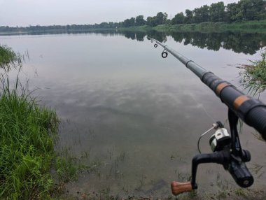 Man fishing in river, first person fishing. Fisherman with rod, spinning reel on the river bank. Sunrise. The concept of a rural getaway.Fisherman holds fishing rod close-up in the first person