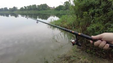 Man fishing in river, first person fishing. Fisherman with rod, spinning reel on the river bank. Sunrise. The concept of a rural getaway.Fisherman holds fishing rod close-up in the first person