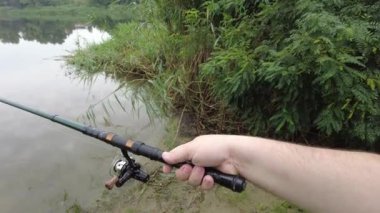 Man fishing in river, first person fishing. Fisherman with rod, spinning reel on the river bank. Sunrise. The concept of a rural getaway.Fisherman holds fishing rod close-up in the first person