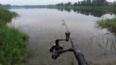 Man fishing in river, first person fishing. Fisherman with rod, spinning reel on the river bank. Sunrise. The concept of a rural getaway.Fisherman holds fishing rod close-up in the first person