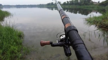 Man fishing in river, first person fishing. Fisherman with rod, spinning reel on the river bank. Sunrise. The concept of a rural getaway.Fisherman holds fishing rod close-up in the first person