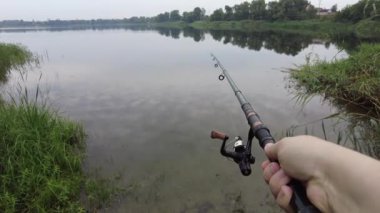 Man fishing in river, first person fishing. Fisherman with rod, spinning reel on the river bank. Sunrise. The concept of a rural getaway.Fisherman holds fishing rod close-up in the first person