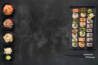 Suşi, soya sosu ve yemek çubuklarıyla servis edilen tahtada, siyah taş desenli arka planda. Uzayın en üst görüntüsü. Japon menüsü