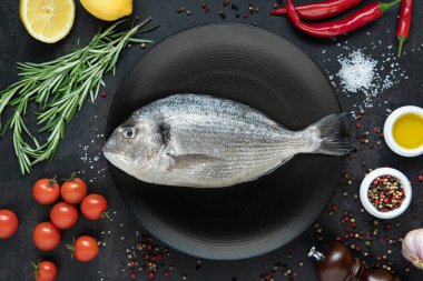 Siyah bir tabakta baharat, biber, biberiye, domates ve koyu arkaplanda limon. Üst görünüm