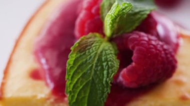 Handheld movement on closeup of raspberries and mint leaves on a slice of cheesecake