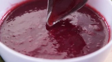 Ladle dipping into bowl of fresh raspberry sauce.