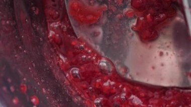 Close up of raspberry sauce being strained through a food mill.