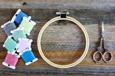 Bobbins of colorful embroidery floss with hoop and sissors on rustic wooden table. Flat lay with copy space in center of hoop