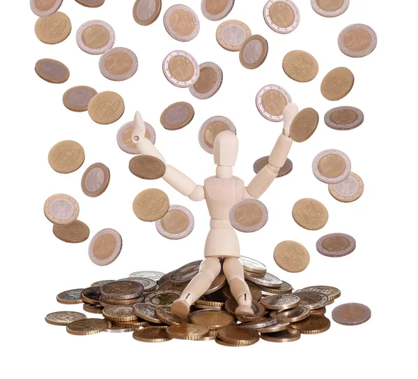 Wooden doll sitting in rain of coins — Stock Photo, Image