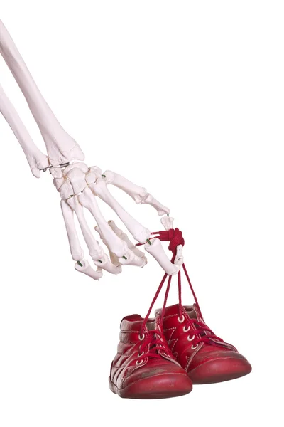 Skeleton hand holding old red baby shoes — Stock Photo, Image