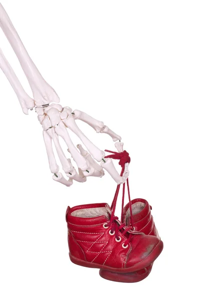 Esqueleto mão segurando velhos sapatos de bebê vermelho — Fotografia de Stock
