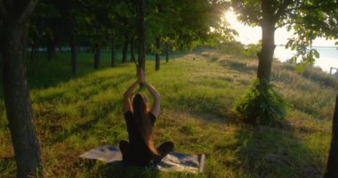 Kız silueti, gün batımında deniz kıyısında yoga yaparken asana 'da oturuyor..