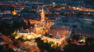 Matthias Kilisesi 'nin aydınlatılmış Balıkçı Kalesi' nde saat kulesiyle uçan 4K İHA. Budapeşte, Macaristan