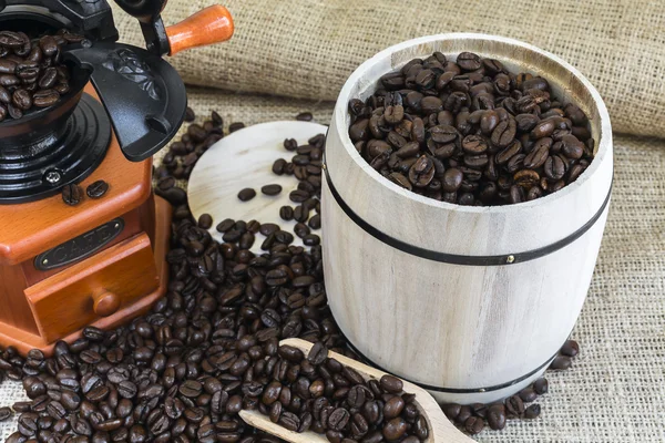 Scattered roasted coffee beans by coffee grinder and wooden barr — Stock Photo, Image