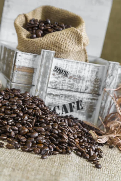 Scattered coffee beans around wooden box with a burlap bag — Stock Photo, Image