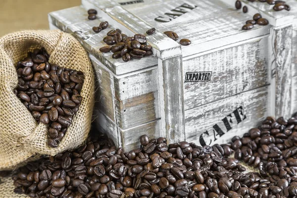 Burlap bag filled with coffee beans beside old wooden box — Stock Photo, Image