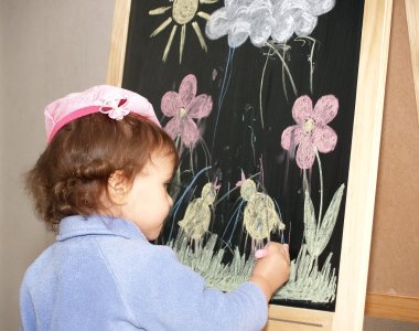küçük kız renk adet tebeşir bir şövale üzerinde çizer.