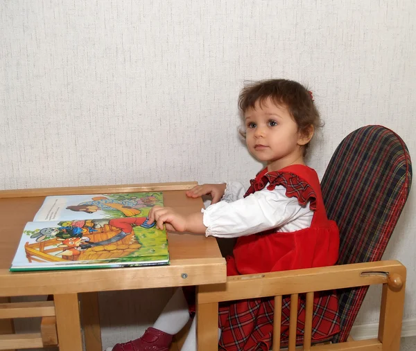 Маленька дівчинка дивиться книгу з кольоровими малюнками — стокове фото