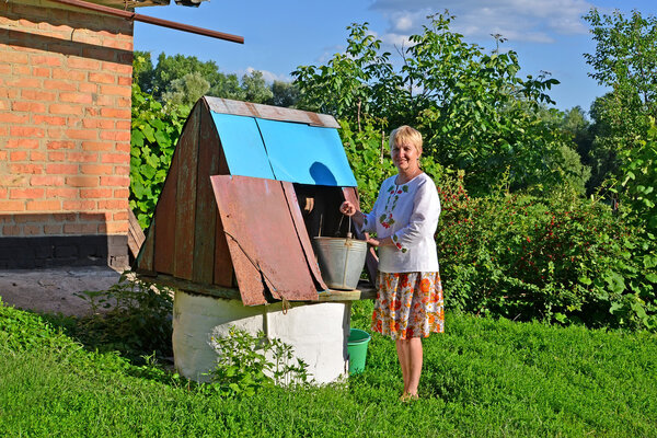 Сельская женщина получает воду из колодца
