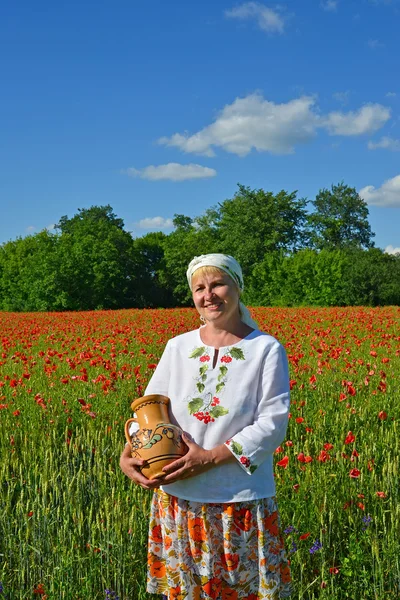 La donna rurale costa con una brocca in un campo di papavero — Foto Stock