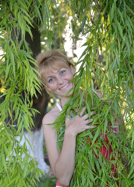 La femme des années moyennes regarde à cause des branches de saule — Photo