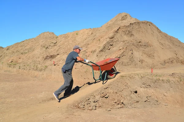 The elderly worker is lucky a wheelbarrow with soil on road cons — Stock Photo, Image