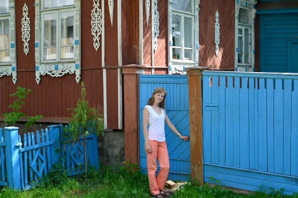 A jovem abre um portão para a casa de madeira com pla esculpida — Fotografia de Stock