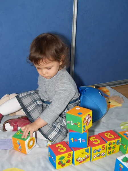 La petite fille joue avec des cubes, assise sur un sol — Photo