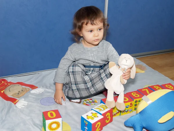 La petite fille joue avec des cubes, assise sur un sol — Photo