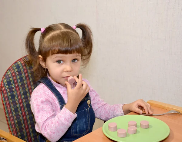The little girl eats sausage with hands — Stock Photo, Image