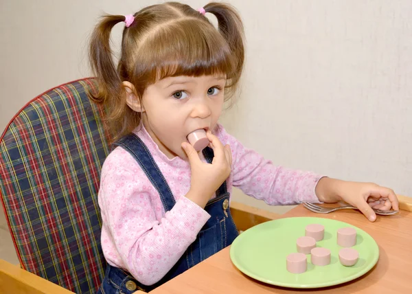 The little girl eats sausage with hands — Stock Photo, Image