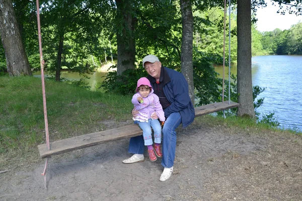 The grandfather with the granddaughter sit on a swing — Stock Photo, Image