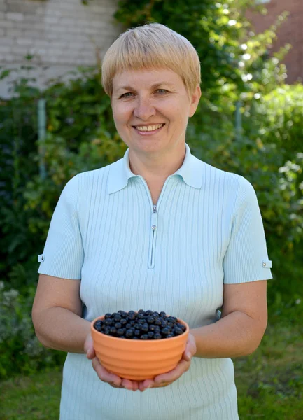 The woman of average years holds in hand a bowl with black curra — Stock Photo, Image