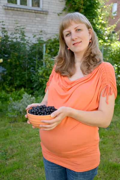 Gravid kvinna håller i hand en skål med svarta vinbär — Stockfoto