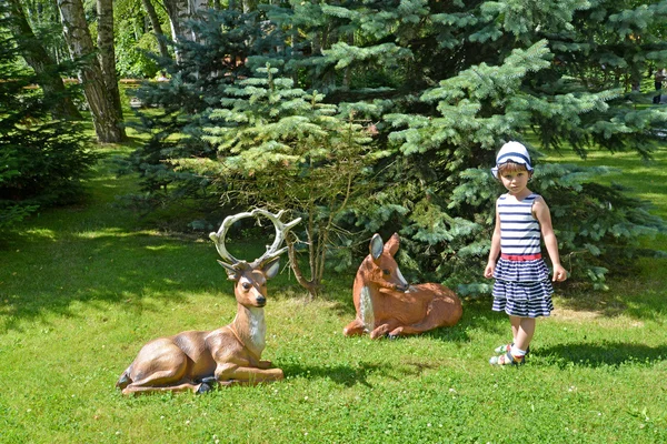The little girl and garden sculptures of deer in a summer garden — Stock Photo, Image