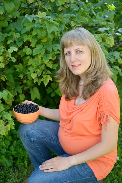 Siyah frenk üzümü bir bahçede bir kase ile hamile kadın — Stok fotoğraf