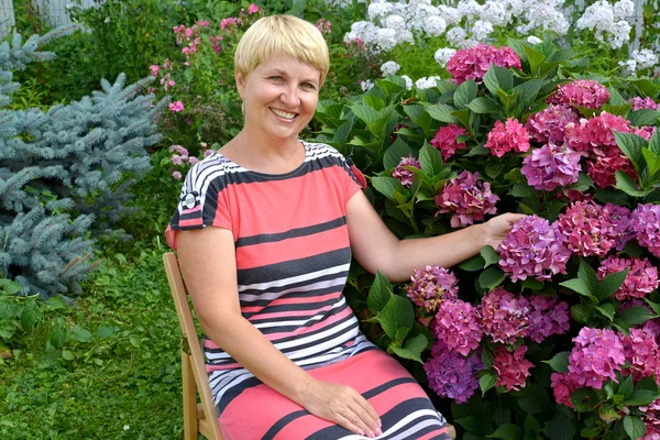 A mulher alegre de anos médios tem um resto em um jardim perto de um — Fotografia de Stock
