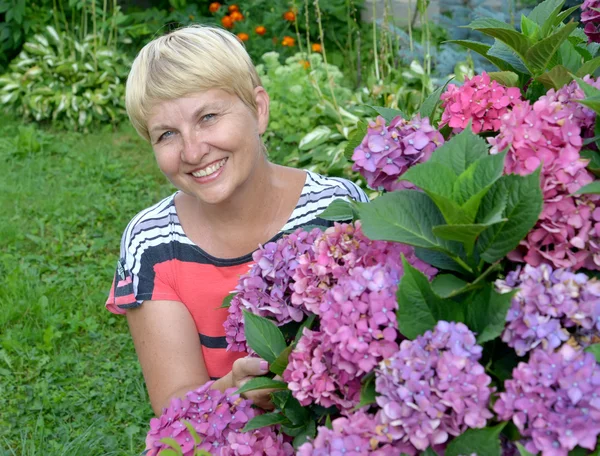 La mujer feliz de los años medios cerca de la hortensia floreciente en — Foto de Stock