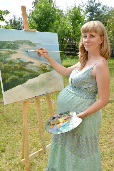 Молода вагітна художниця пише фотографію олійною фарбою — стокове фото