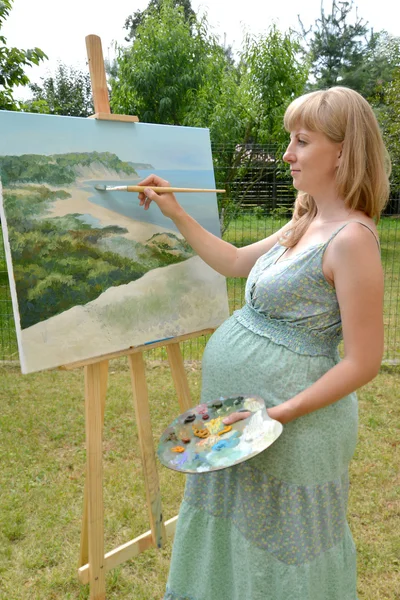 The young pregnant female artist writes a picture with oil paint — Stock Photo, Image