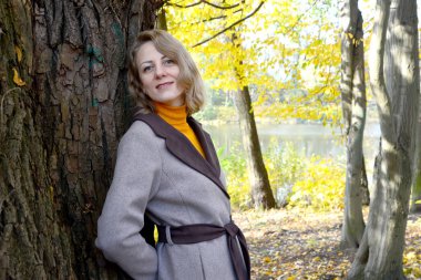 Kadın yaşlı bir ağacın gövdesine yaslandı. Autumn Park