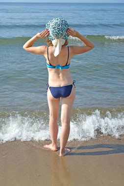 Hasır şapkalı ve mayo giymiş bir kadın sırtı Baltık Denizi 'nin kumlu sahilinde duruyor. Kalininingrad bölgesi