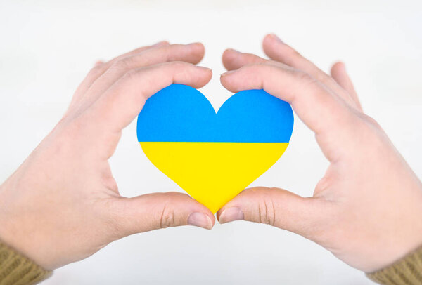 heart in colors of ukrainian flag in hands, concept of help and support for ukraine