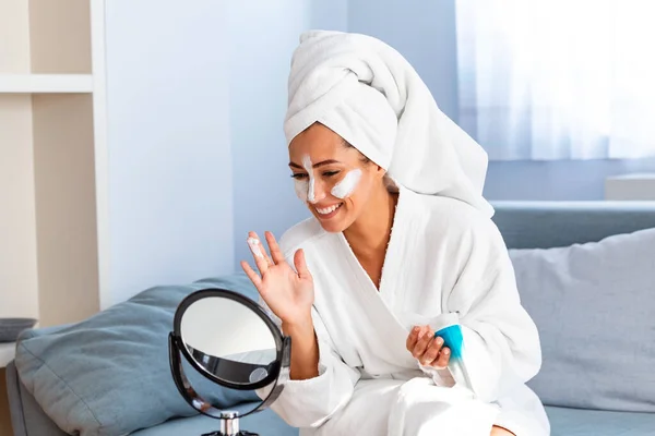 So beautiful. Close-up of girl with beauty mask on her face looking in mirror. Girl uses natural mask. Attractive young woman sitting with a facial mask on her skin